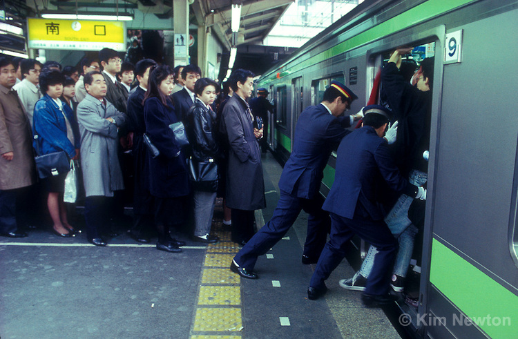 Japanese commuters wait in line for the next train, while people pushers push passengers onto the Yamanote line subway train during the morning rush hour at Shinjuku station in Tokyo, Japan. The daily ritual is performed to maximize the number of commuters on trains.