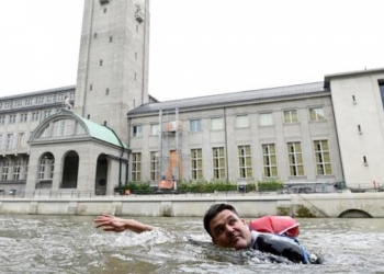 Cansado do tráfego, ele nada para o trabalho com notebook e terno na mochila