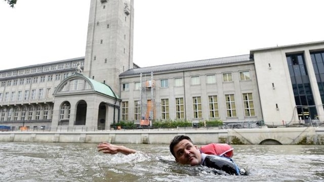 Cansado do tráfego, ele nada para o trabalho com notebook e terno na mochila